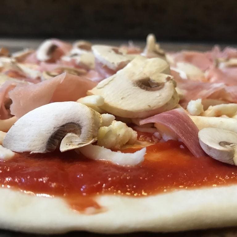 Pizza con prosciutto crudo e funghi in preparazione