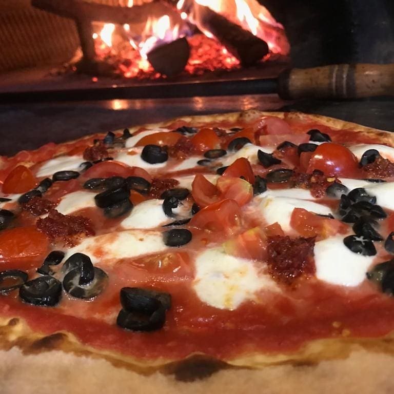 Pizza con olive e pomodorini nel forno a legna
